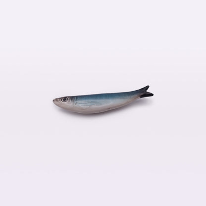 A realistic ceramic model of a fish, resembling a hand-made Portuguese ceramic sardine, mainly blue-gray in color with a white underbelly, lying against a plain light background—this is the Ceramic Sardine Fridge Magnet by Tejo Shop.