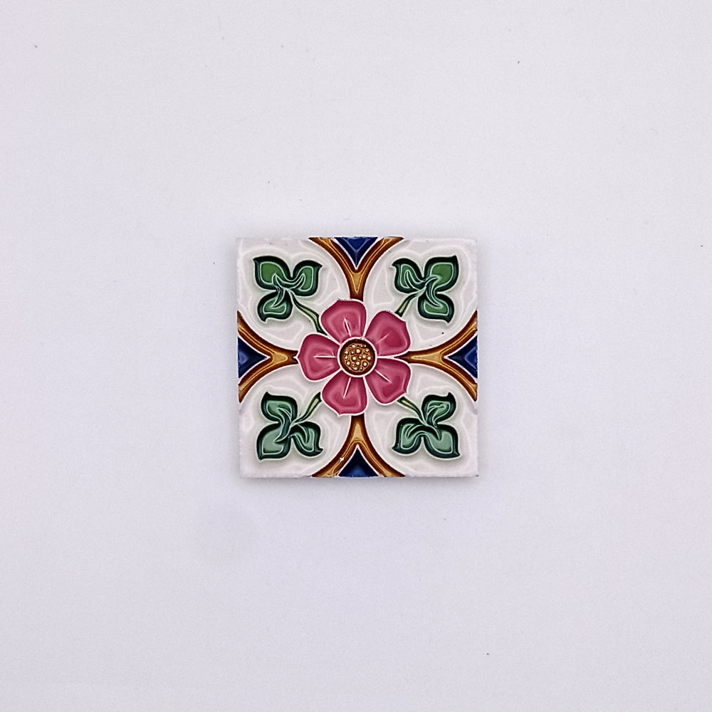 Decorative Mediterranean small ceramic tile featuring a floral design with a central pink flower surrounded by green leaves and geometric patterns in blue, orange, and white against a neutral backdrop from Tejo Shop.