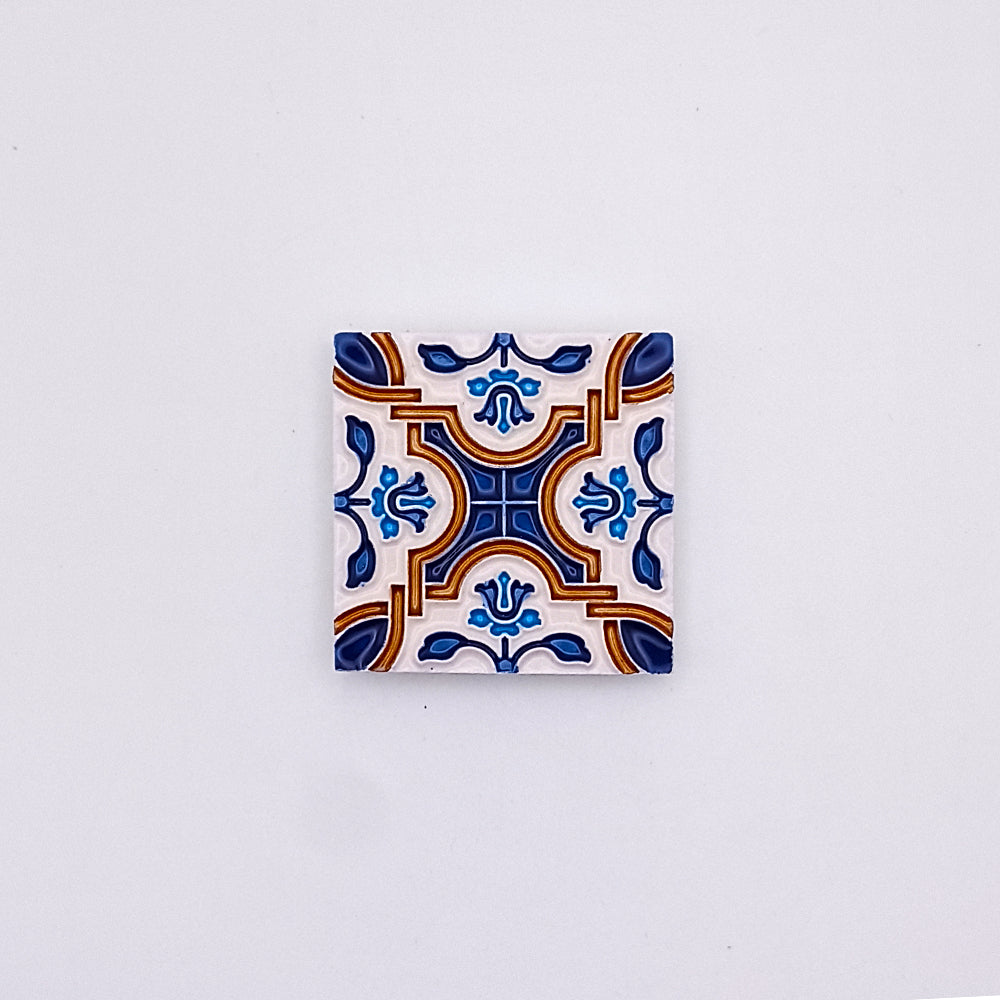 Decorative Mediterranean Hand Made Ceramic Tile with a symmetrical pattern in blue, orange, and white, centered on a plain, pale background from Tejo Shop.