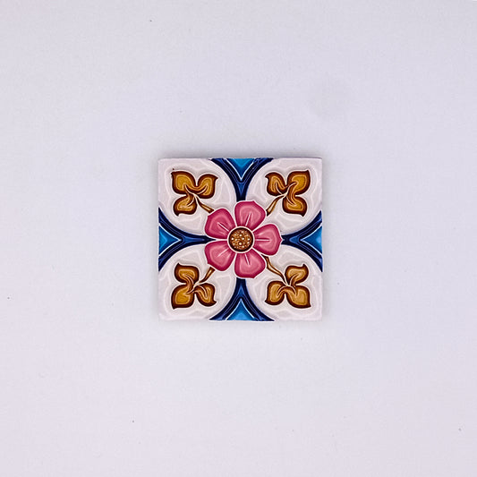 Square decorative hand-painted Tejo Shop small ceramic tile with a central pink flower design, surrounded by blue and gold patterns on a white background.