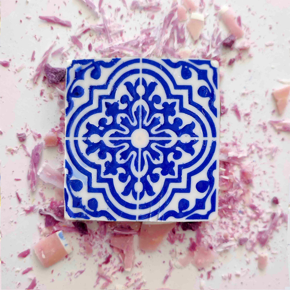 The Lisbão Rosa de Azulejo soap, handmade with a blue and white geometric Portuguese tile design, is displayed on a surface sprinkled with pink and purple candy or chocolate shavings.