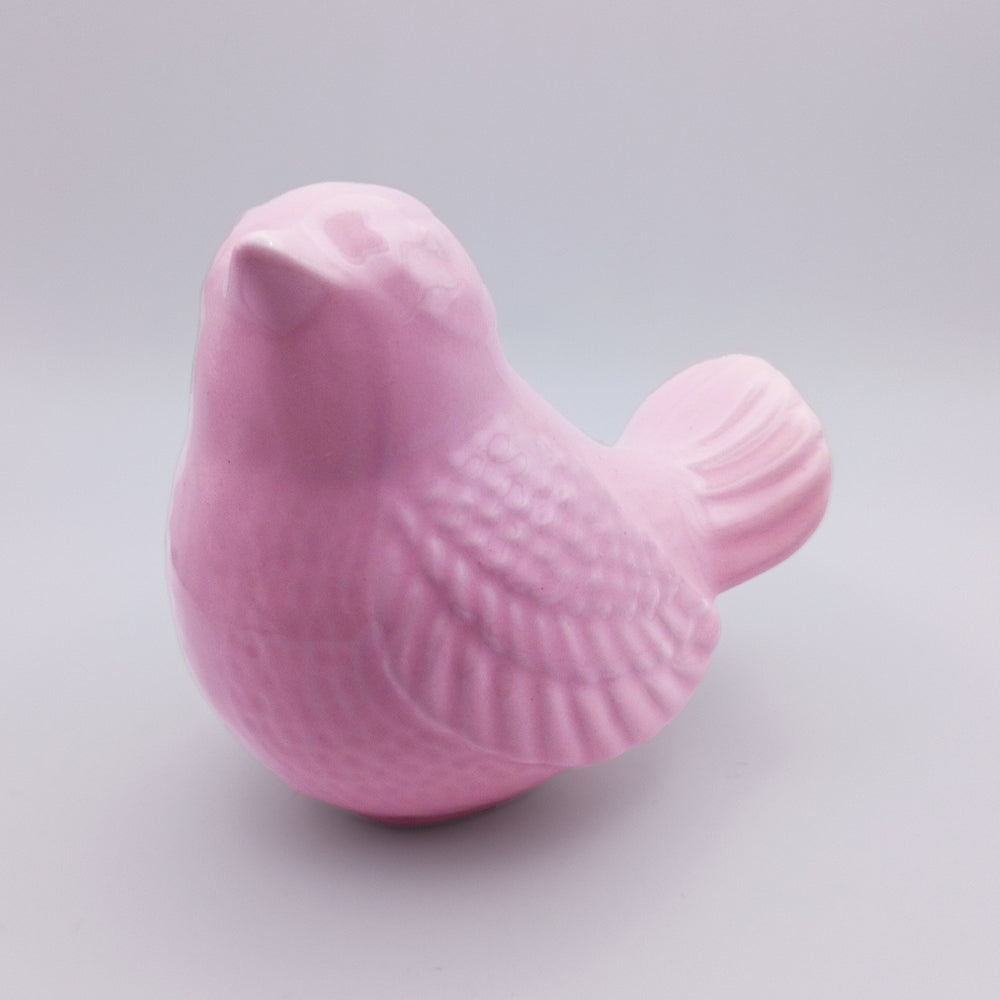 The Tejo Shop's Ceramic Bird looking up Figurine in a charming pink hue is showcased against a plain light gray background. It features a round body, short tail, and intricately etched feathers, making it an enchanting piece of home decor.