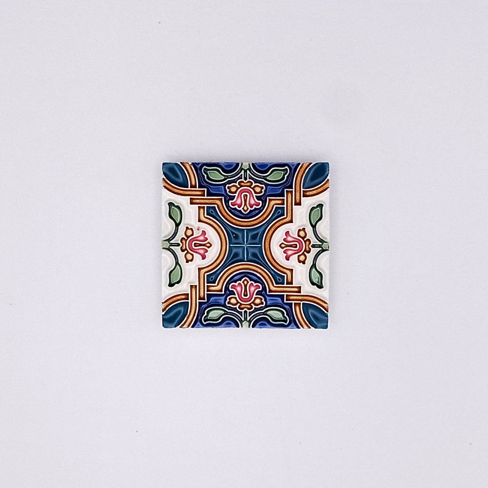 A small square Traditional Ceramic Small Tile with a colorful, symmetrical floral pattern on a white background. The design features blue, green, red, and yellow accents, embodying Portuguese sophistication from Tejo Shop.