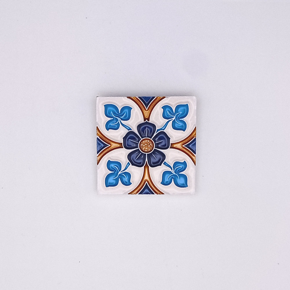 A decorative Tejo Shop Portuguese art tile featuring a symmetrical floral design in blue, white, and brown, centered with a small golden embellishment, against a plain light gray background.