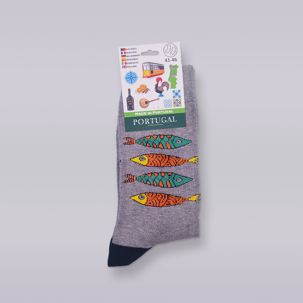 The Portuguese Sardines Special Edition socks by Tejo Shop feature a vibrant fish pattern on a gray background, made from high-quality cotton. The packaging highlights iconic Portuguese symbols, including a tram, pastries, and a rooster, with text that reads "Made in Portugal" and notes sizes 41-46.