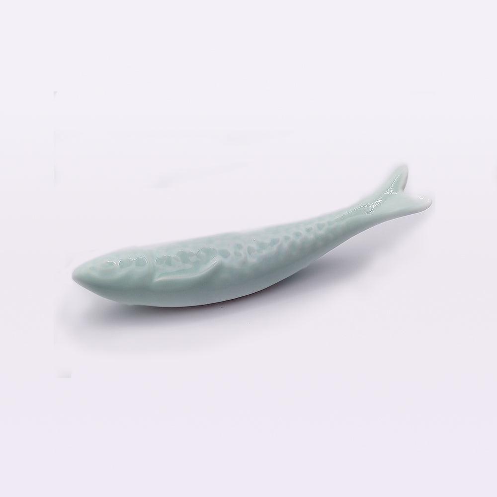 A Tejo Shop Portuguese Ceramic Sardines, painted in light blue, is placed on a white surface. Reflecting traditional craftsmanship, the detailed scales and fins are reminiscent of handcrafted Portuguese ceramics, designed to hold chopsticks when not in use.