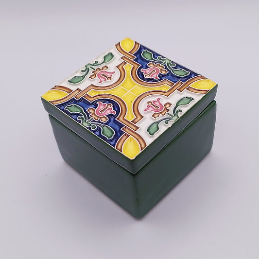 A small square green Peniche Ceramic Box from Tejo Shop with a decorative lid featuring a colorful mosaic design. The lid includes red flowers, green leaves, and elaborate patterns in yellow, blue, and white. The background is plain and light gray, adding timeless beauty to your home elegance.