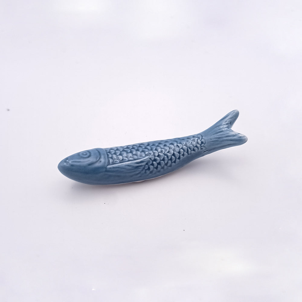 Displayed on a plain white background, the Ceramic Sardine Fridge Magnet from Tejo Shop showcases a small, ceramic, fish-shaped figurine in solid blue. Its surface is intricately detailed with scales and fins, creating a realistic and textured appearance. This eye-catching piece of kitchen decor beautifully nods to Portuguese icons.