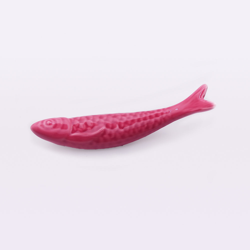 A pink, ceramic, fish-shaped object on a plain white background. The fish detail includes scales, a fin, and a tail. The object reflects the traditional craftsmanship of Portugal and has a glossy finish. This is the **Portuguese Ceramic Sardines** from **Tejo Shop**.