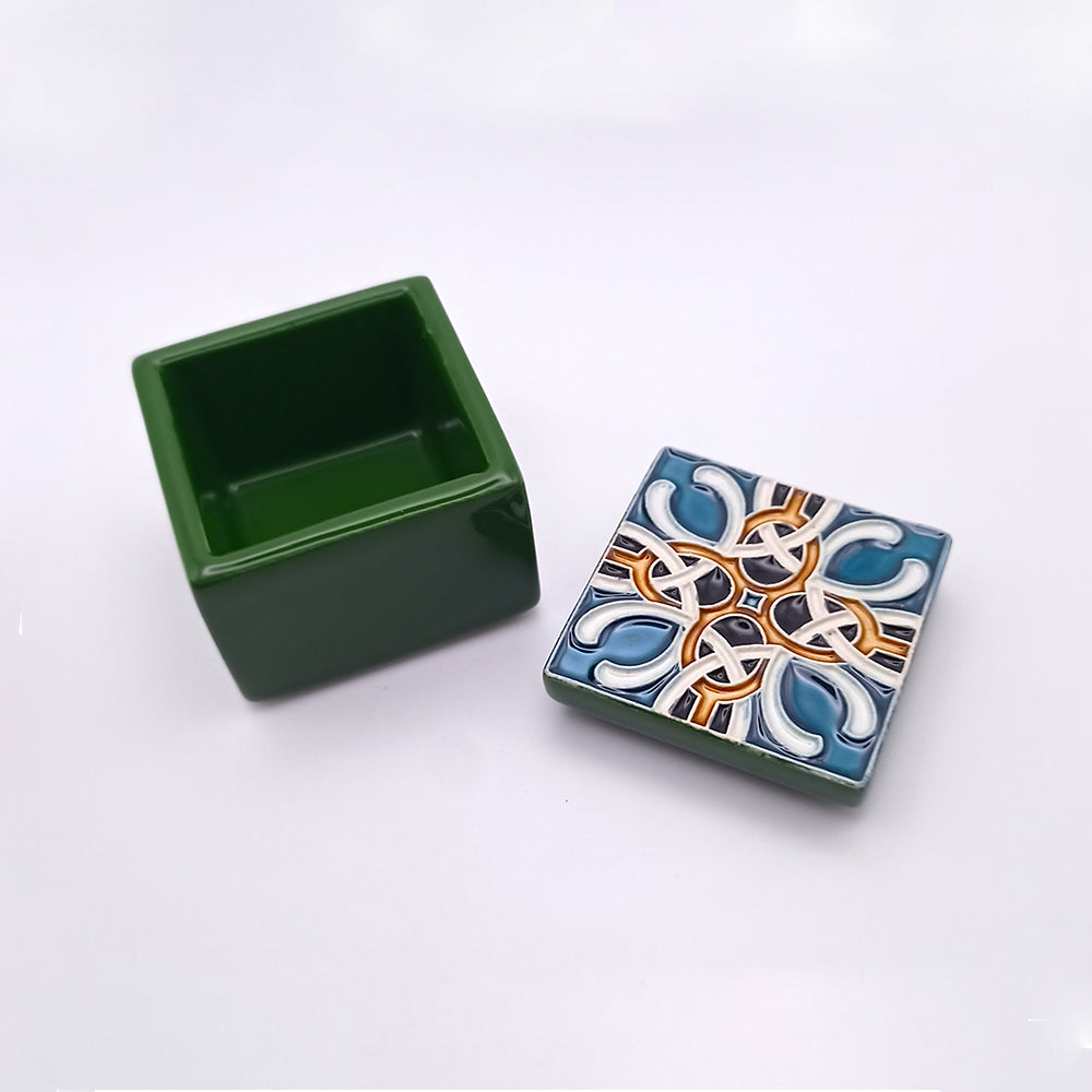 A small, square, green ceramic box with its lid placed beside it. The lid features an intricate, colorful pattern with blue, white, and orange designs. The inner compartment of the luxurious Ponta Delgada Ceramic Box by Tejo Shop is empty, and both pieces are set against a plain white background.