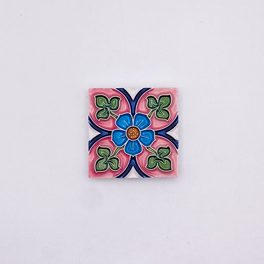 Decorative Spanish Tiles from Tejo Shop featuring a colorful floral design with blue, pink, and green petals, centered around a small orange dot, against a grey background, adding an artistic flair.
