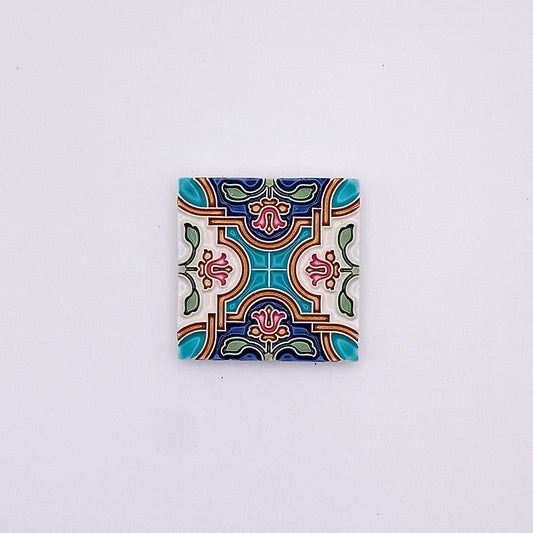 A square Tejo Shop Spanish Small Tile with a colorful, intricate symmetrical pattern, featuring bold shapes and colors such as teal, red, yellow, and green on a white background.
