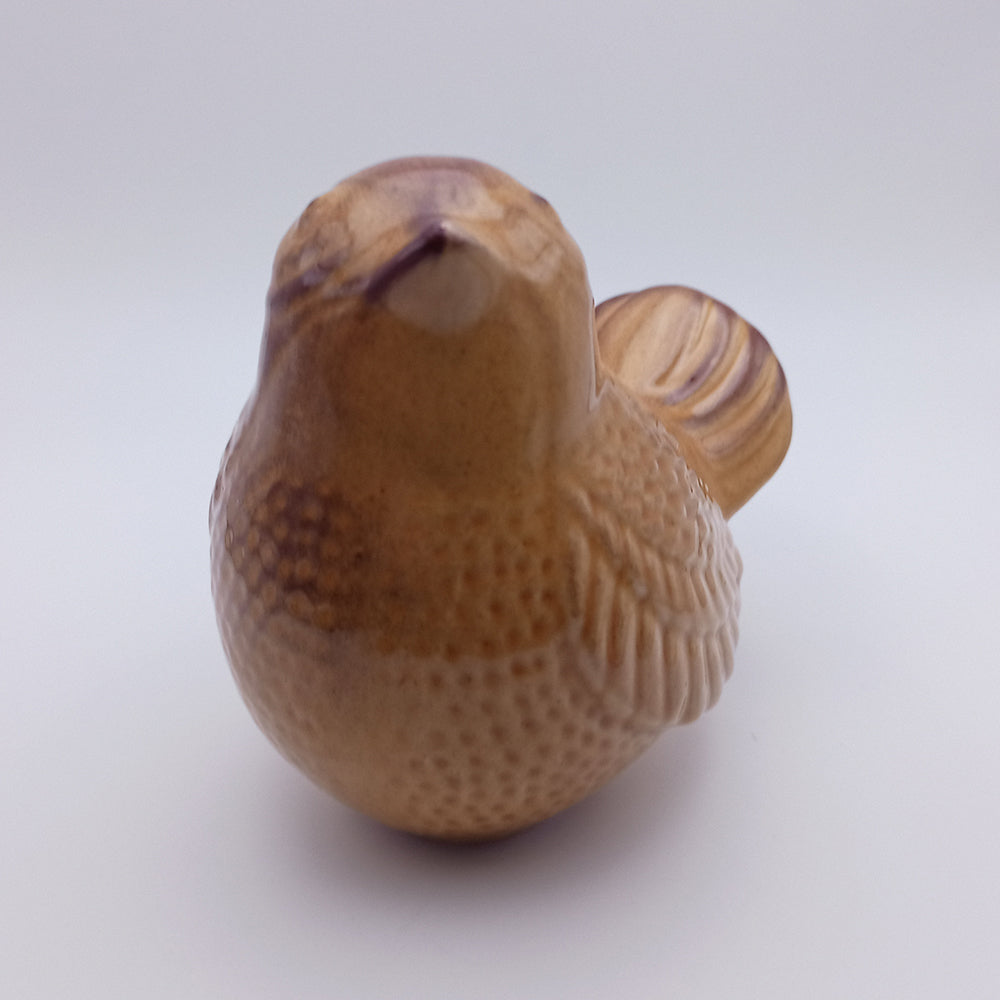 Introducing the Ceramic Bird looking up Figurine from Tejo Shop. This small, handmade brown ceramic bird figurine features subtle texturing on its wings and body, showcasing detailed craftsmanship. Perfect as home decor, the bird is positioned looking upward against a plain light background.