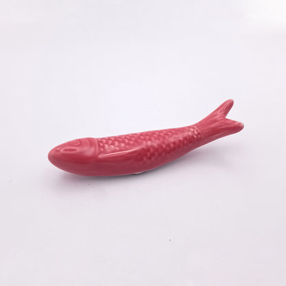 A Ceramic Sardine Fridge Magnet by Tejo Shop is positioned against a plain white background. The textured surface and smooth edges create an appealing look, making it a perfect kitchen decor item. This red, fish-shaped decorative piece features well-defined fins, tail, and head, embodying the charm of a Portuguese icon.