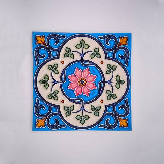 A colorful hand-painted Tejo Shop ceramic tile featuring a symmetrical design with a pink flower at the center, surrounded by blue and green floral patterns, set against a white background.