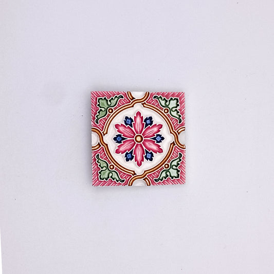 A vibrant, square ceramic tile with a detailed Small Spanish Tile Pattern in pink, red, green, and white, centered on a light gray background by Tejo Shop.