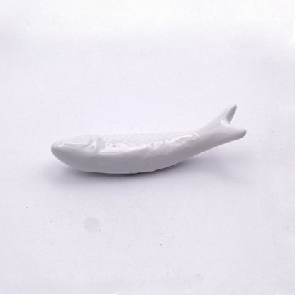 A white, fish-shaped ceramic chopstick rest is placed against a plain white background. The rest is minimalist in design, echoing the charm of Tejo Shop's Ceramic Sardine Fridge Magnet, with subtle detailing to suggest the fish's body and fins, making it an ideal piece for sophisticated kitchen decor.